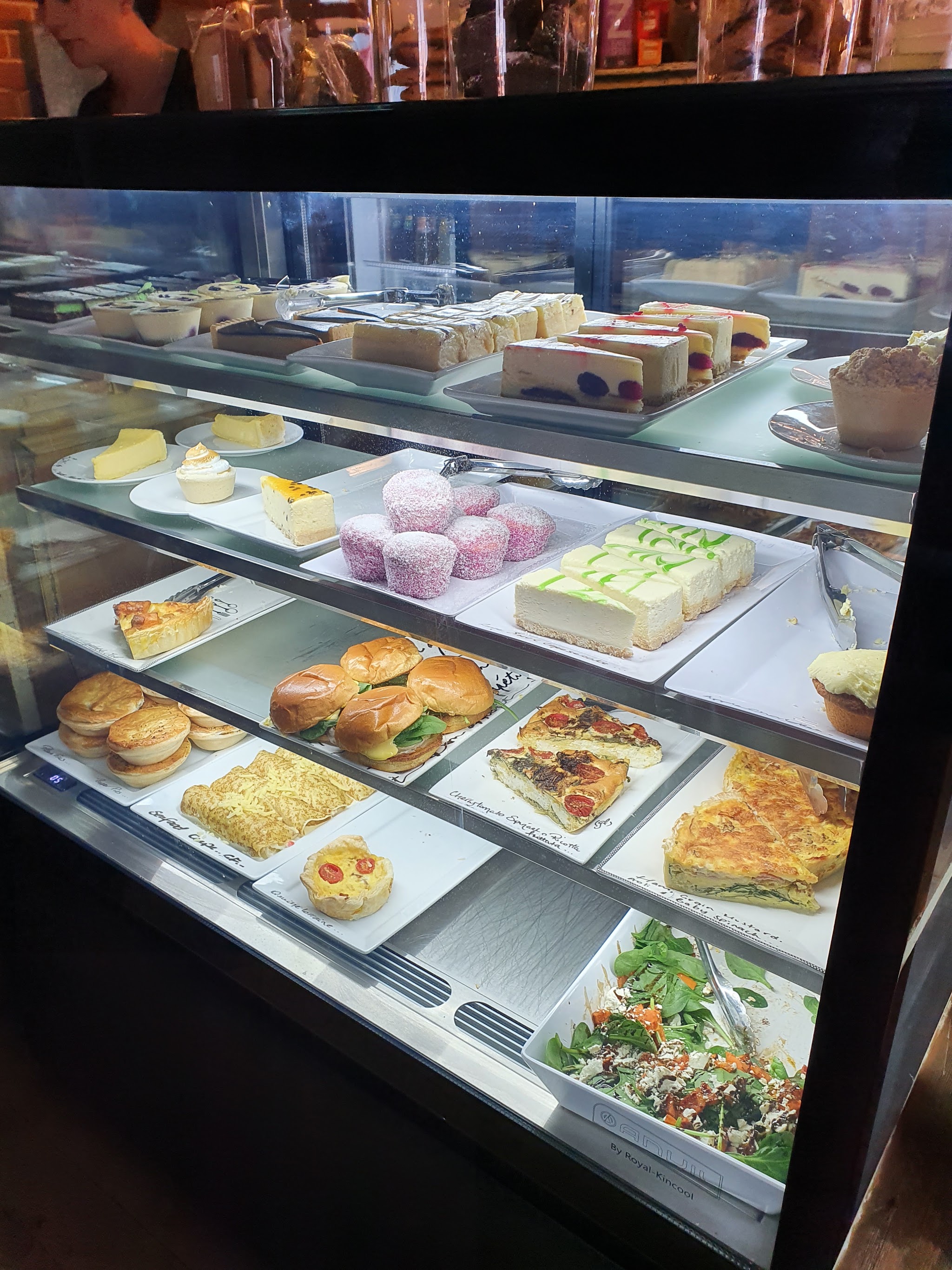 The cake cabinet with slices, cheesecakes, lamingtons, quiches, sliders and pies